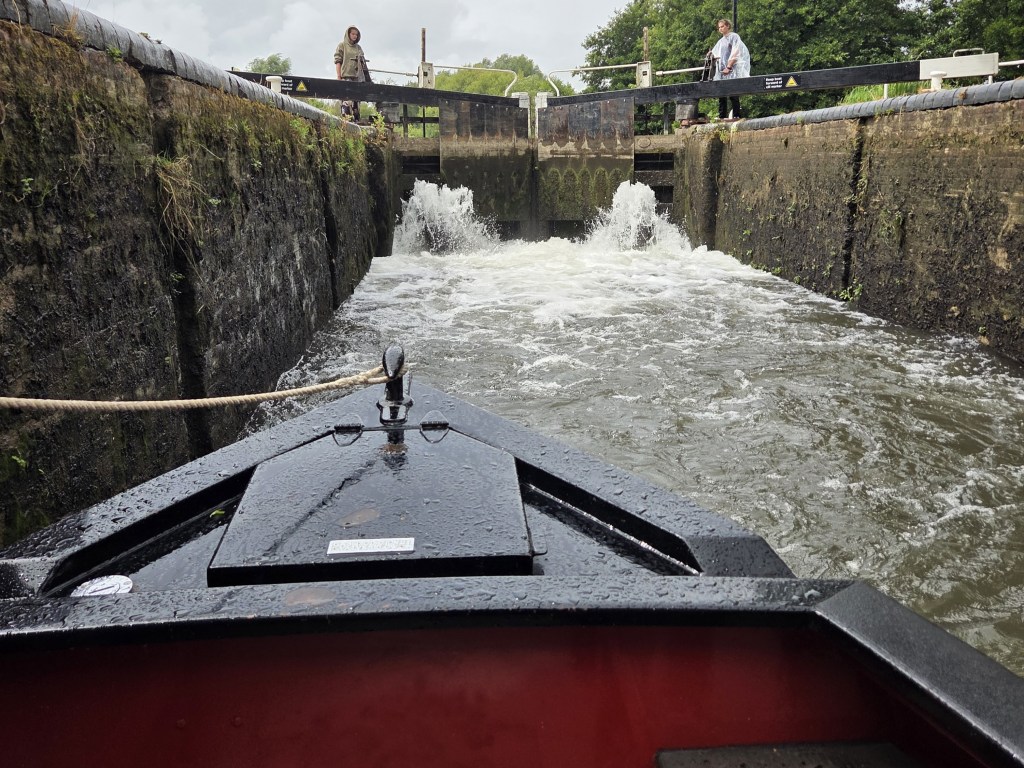 narrowboat entering a lock, with crewmates pushing a heavy wooden gate.